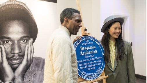 Poet Lemn Sissay and Qian Zephaniah stand either side of a blue plaque which commemorates poet Benjamin Zephaniah. The plaque reads: The people's poet Benjamin Zephaniah 1958 - 2023. Writer, activist, actor, musician. His creative voice travelled from Birmingham around the world.